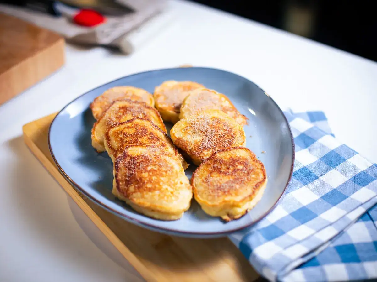 Tortitas de manzana doradas y espolvoreadas con azúcar y canela, servidas en un plato azul.