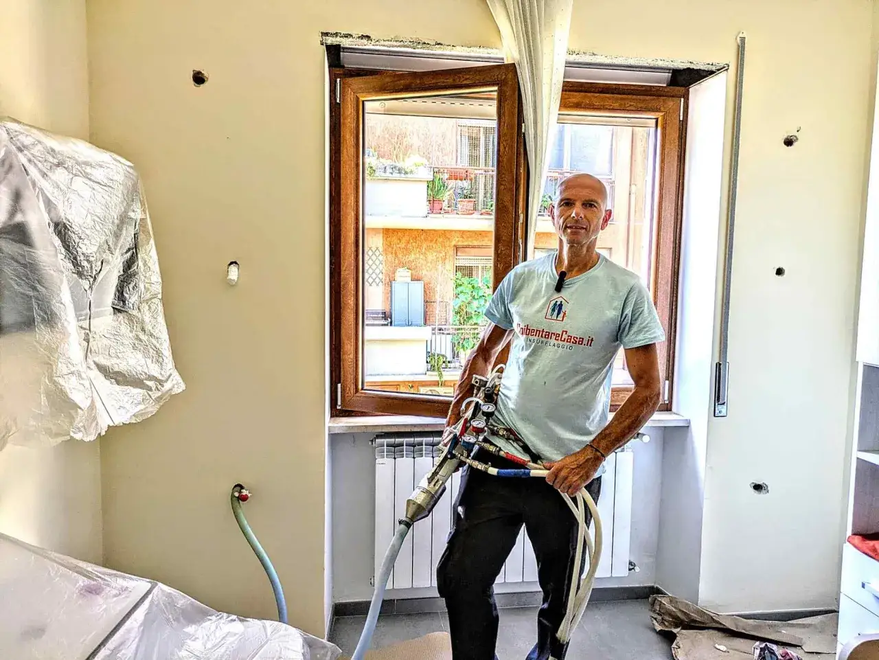 Un uomo con un'attrezzatura per l'insufflaggio mostra come riscaldare una stanza freddissima, isolando le pareti.
