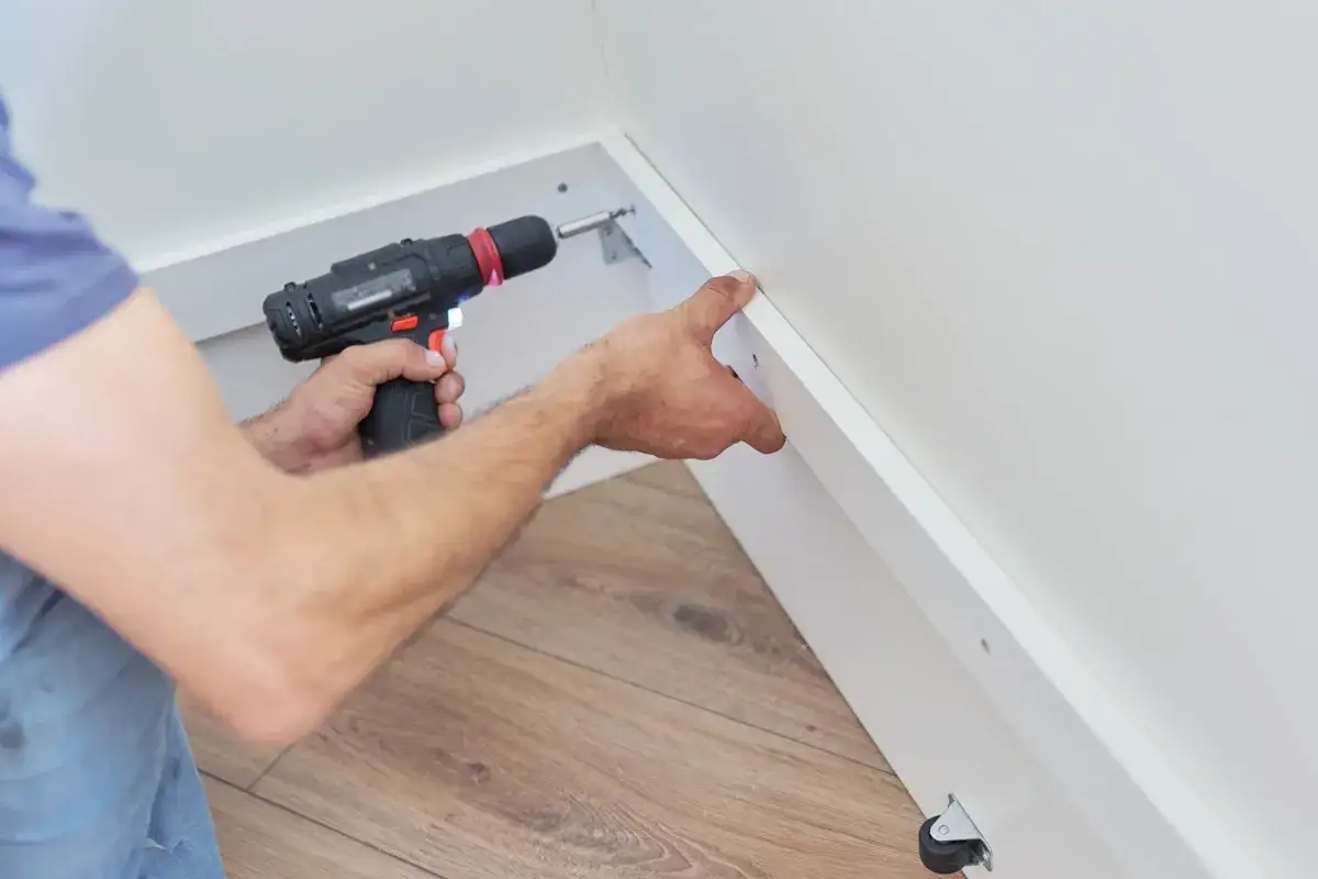 Pose d'un placo sur ossature bois. Un artisan utilise une visseuse pour fixer une plaque blanche.