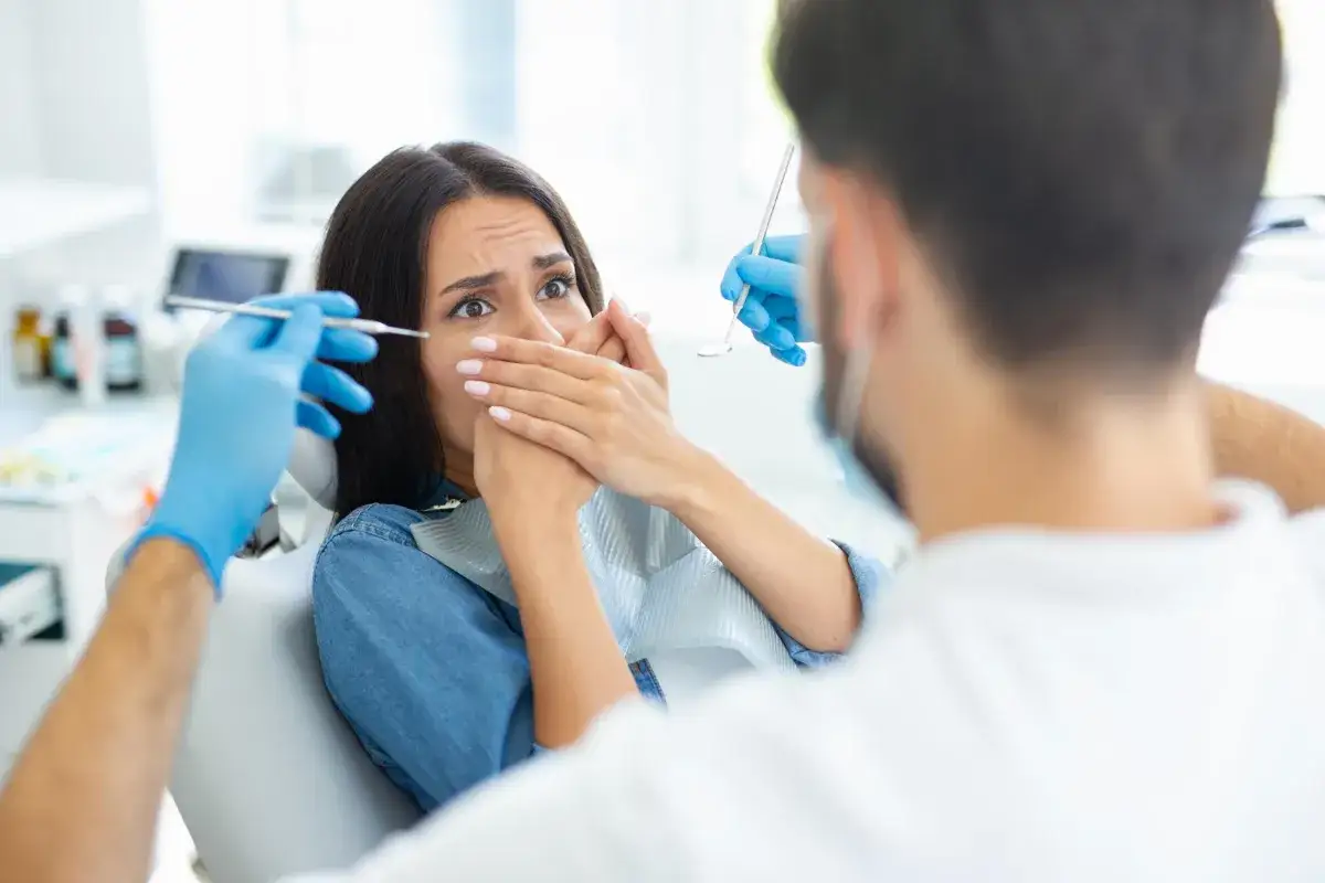 Przerażona pacjentka z dentofobią zakrywa usta przed dentystą.