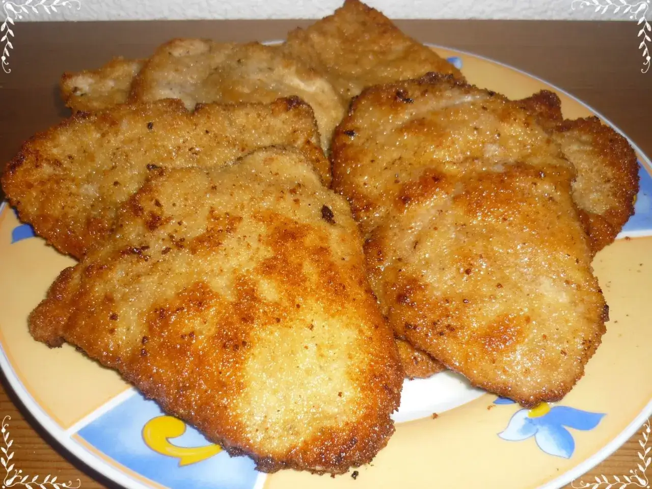 Mehrere goldbraune Wiener Schnitzel liegen auf einem Teller mit Blumenmuster.