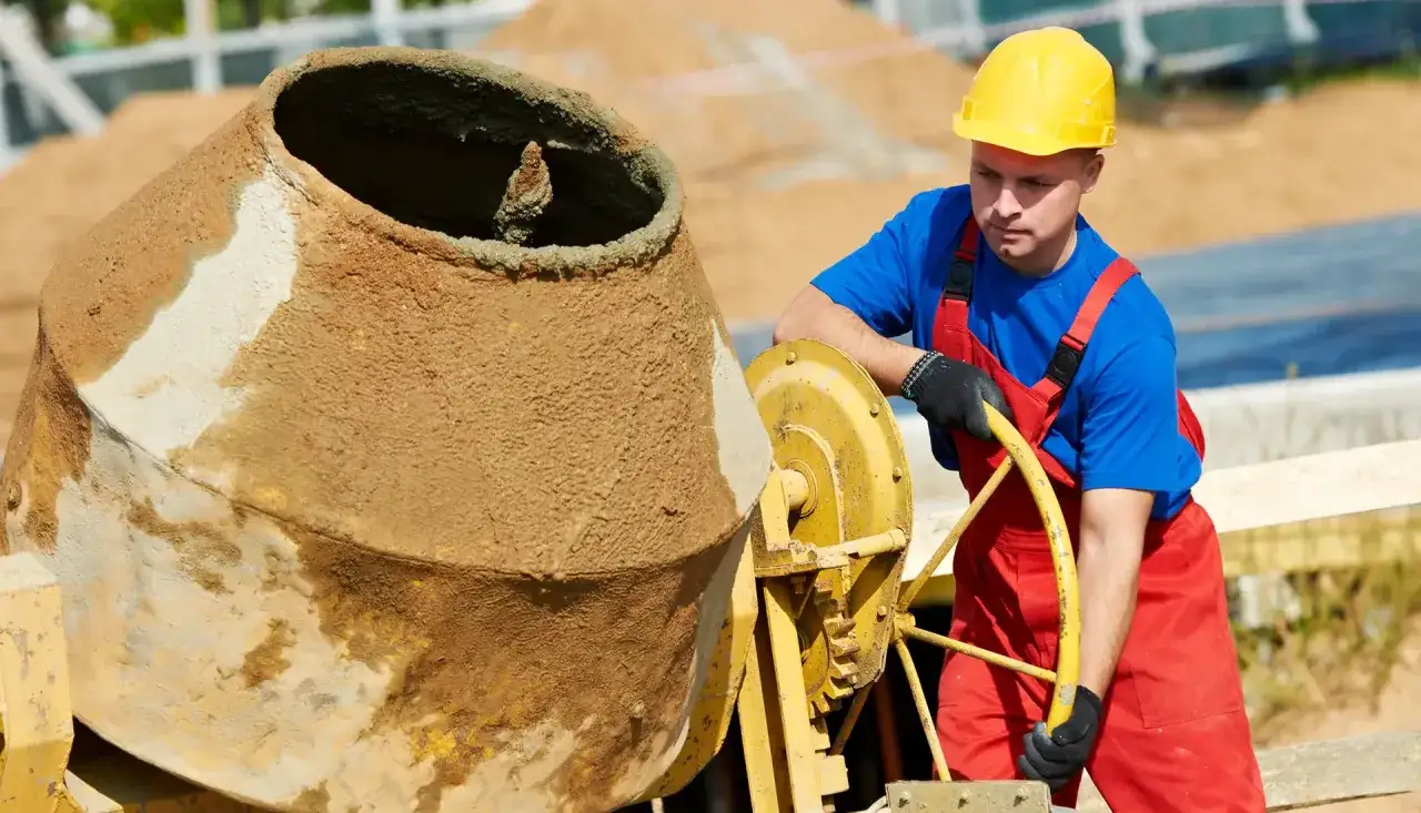 Obrero con casco amarillo operando una hormigonera, mostrando uno de los tipos de hormigoneras usadas en construcción.