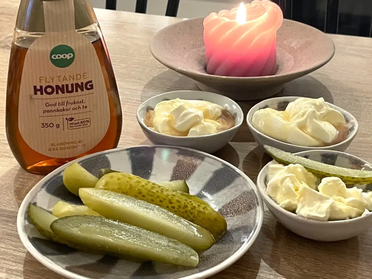 Saltgurka, smetana och honung p&aring; bordet, med en t&auml;nd ljuslykta i bakgrunden.