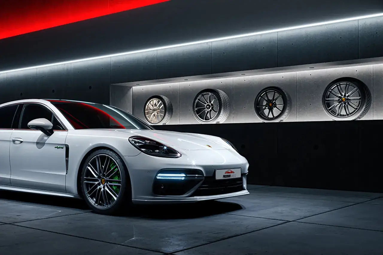Weißer Porsche mit teuren Felgen und vier ausgestellten Rädern an der Wand.
