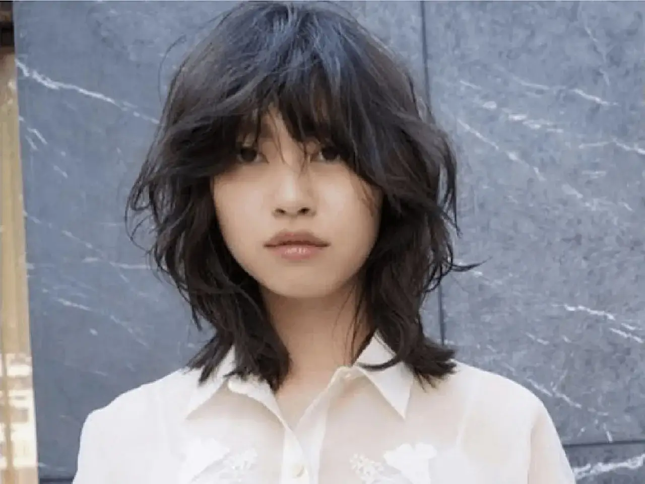 Mujer con un corte de pelo wolf cut, con capas desordenadas y flequillo que le cubre los ojos.