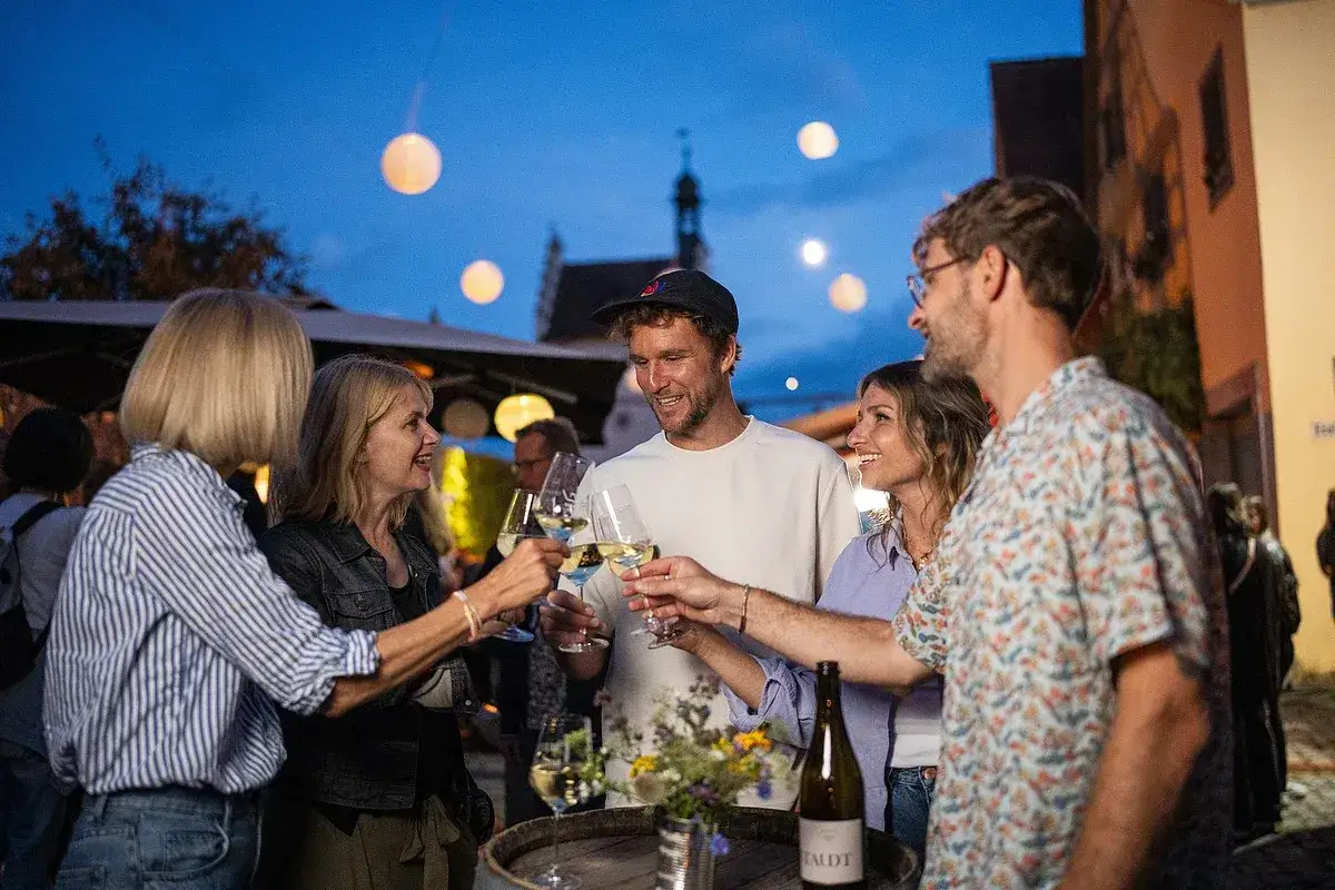 Freunde stoßen auf einem Weinfest in Franken an. Die Abendstimmung mit Lampions und fränkischer Gemütlichkeit.