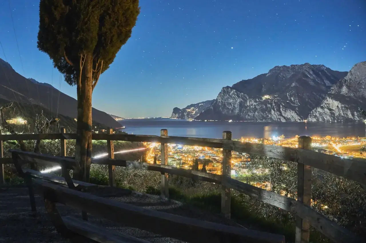 Peschiera del Garda di sera: un panorama mozzafiato con luci scintillanti, montagne maestose e un cielo stellato. Ideale per una serata romantica.