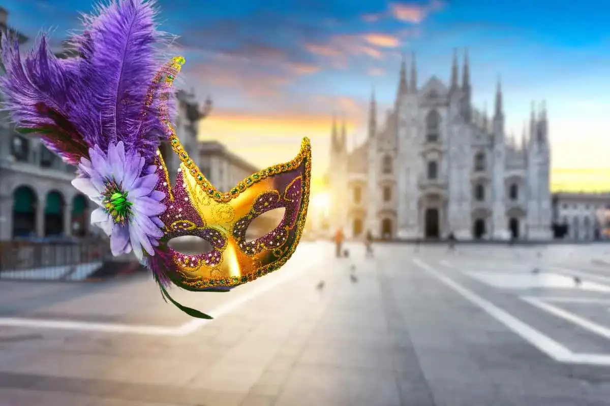 Maschera dorata e viola con piume, in primo piano, con il Duomo di Milano sullo sfondo al tramonto.