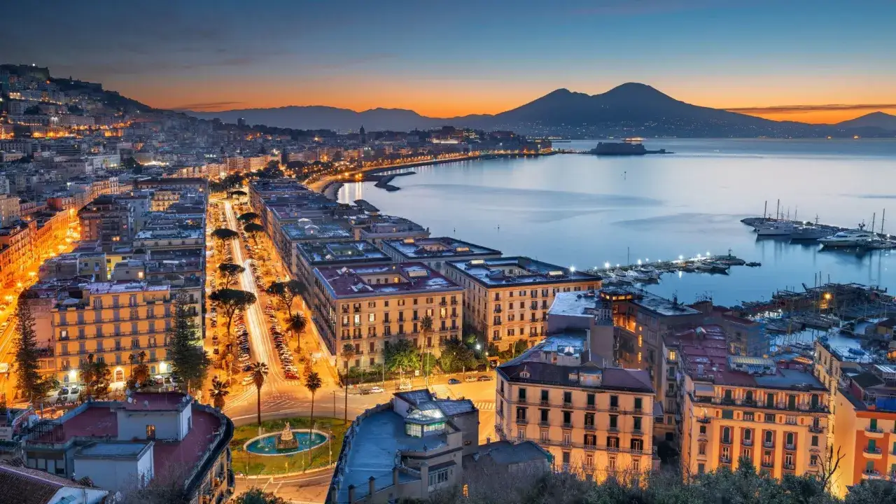 Abenddämmerung über Napoli, Italien. Der Vesuv wacht über die beleuchtete Stadt und den glitzernden Golf.