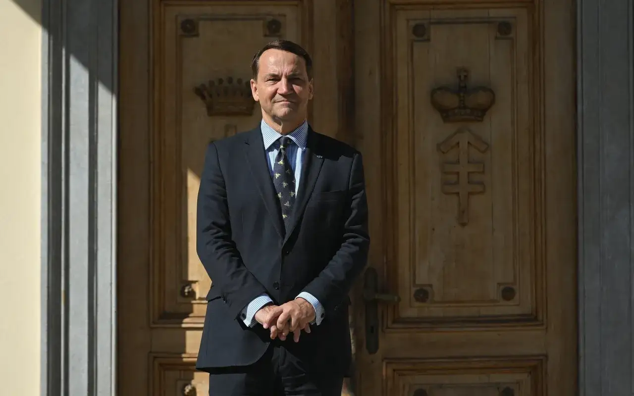 Radosław Sikorski, polityk Platformy Obywatelskiej, stoi przed ozdobnymi drzwiami.