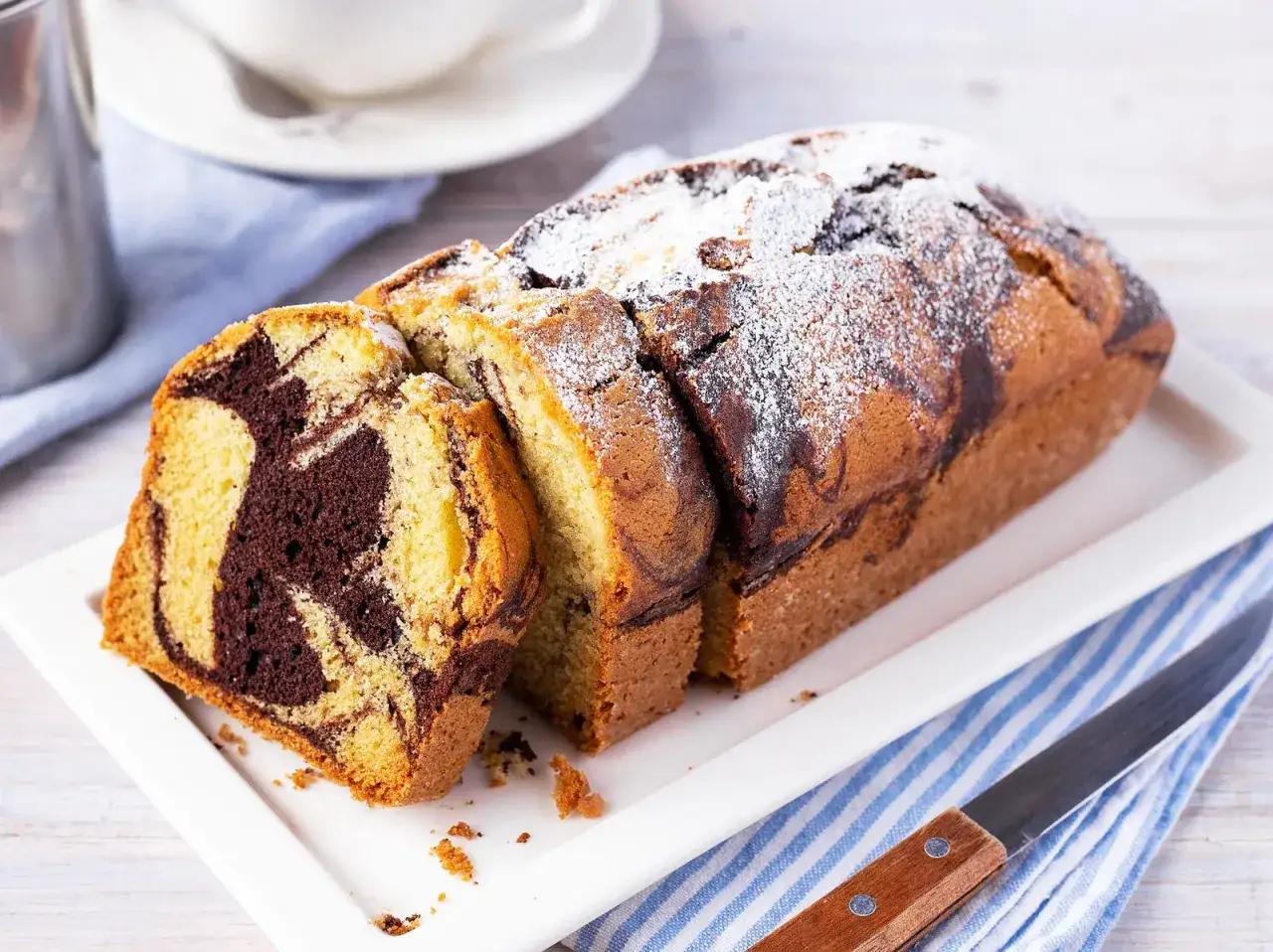 Der beste Marmorkuchen, frisch gebacken und mit Puderzucker best&auml;ubt, liegt auf einer wei&szlig;en Platte.