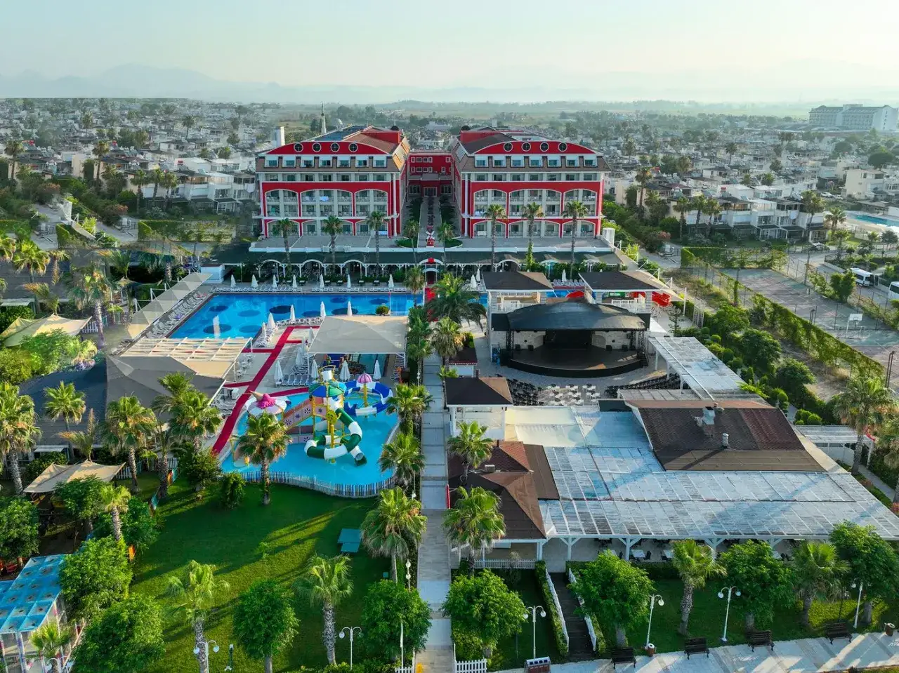 Widok z lotu ptaka na kompleks hotelowy w Belek, z basenami, zjeżdżalniami wodnymi i sceną. Idealne miejsce na wakacje w Orange County Belek.