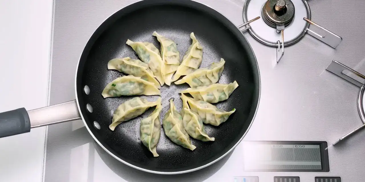 Gyoza vegetarisch braten in einer Pfanne. Die gef&uuml;llten Teigtaschen sind kreisf&ouml;rmig angeordnet und werden gerade zubereitet.