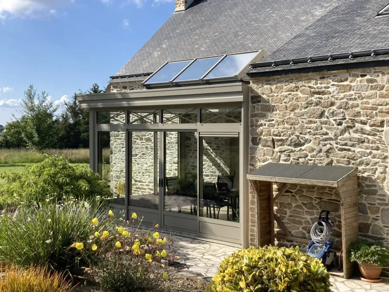 Belle extension maison en pierre avec un puit de lumière, offrant une vue sur le jardin fleuri.