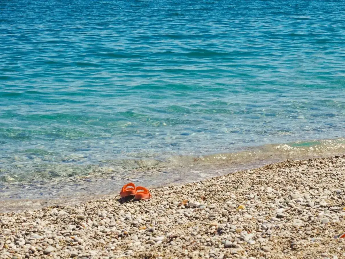 Chanclas naranjas abandonadas en la **playa Malvarrosa de Corinto**, esperando a su dueño junto a las aguas cristalinas.