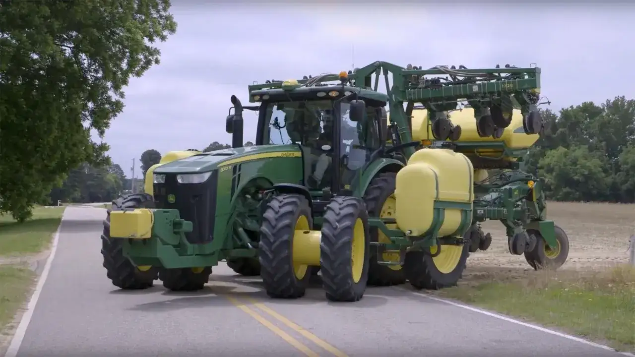 A green John Deere tractor with yellow tanks and planters attached drives on a road, reminding us of important harvest safety tips.