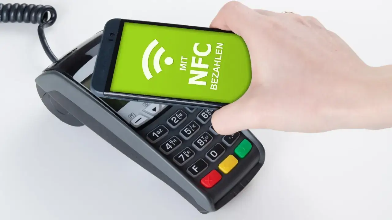 Hand h&auml;lt Smartphone &uuml;ber ein Kassenterminal f&uuml;r mobiles Bezahlen mit NFC.
