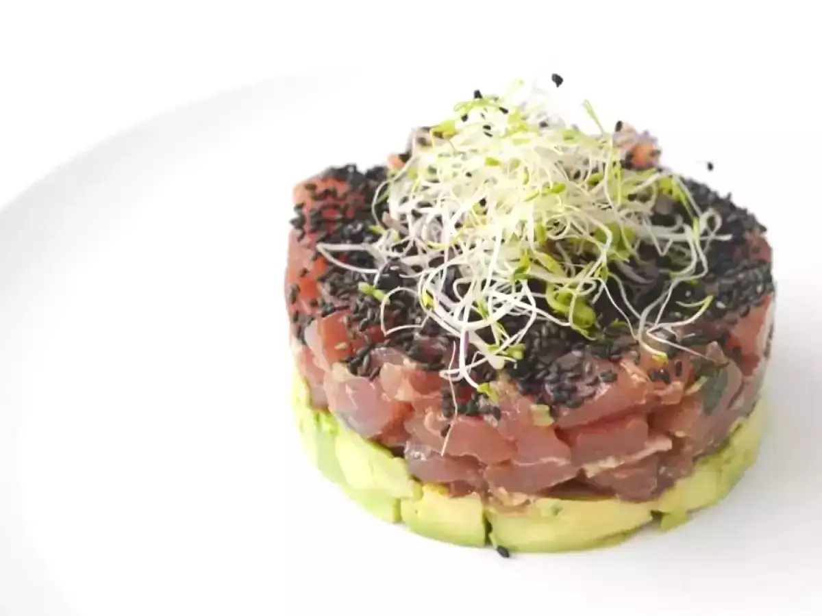 Un d&eacute;licieux tartare de thon, joliment dress&eacute; sur un lit d'avocat, parsem&eacute; de graines de s&eacute;same noir et garni de pousses fra&icirc;ches.