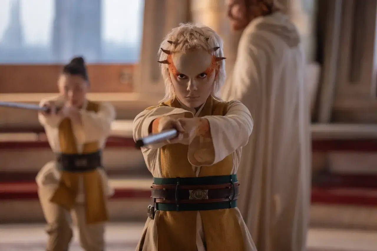 Młoda **star wars acolyte** z rogami na głowie i pomarańczowymi zdobieniami twarzy ćwiczy z mieczem świetlnym.