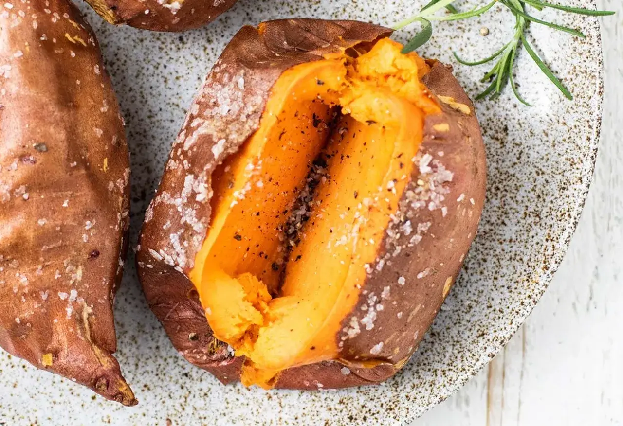 Patate dolci al forno, aperte a metà, condite con sale grosso e pepe, su un piatto con rosmarino.
