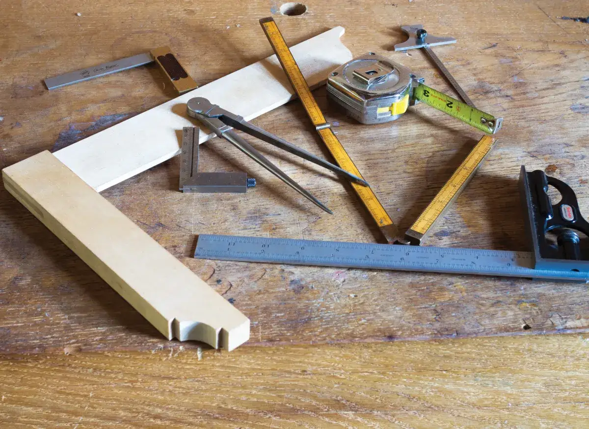 Outils de menuiserie sur un &eacute;tabli en bois, pr&ecirc;ts &agrave; couper du bois. &Eacute;querres, compas, m&egrave;tres et r&egrave;gles sont dispos&eacute;s autour de pi&egrave;ces de bois.