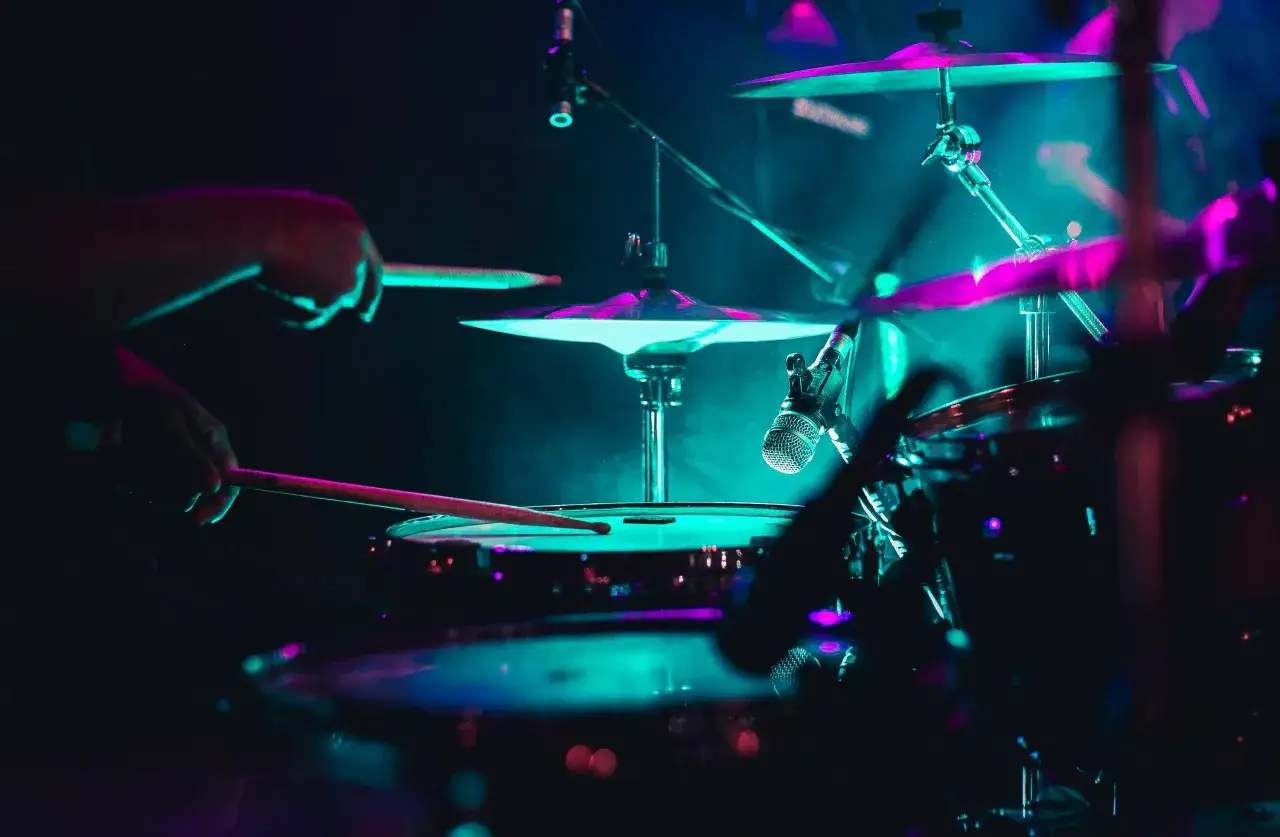 Greyson Nekrutman schl&auml;gt mit Drumsticks auf ein Schlagzeug, beleuchtet von blauem und pinkem Licht.