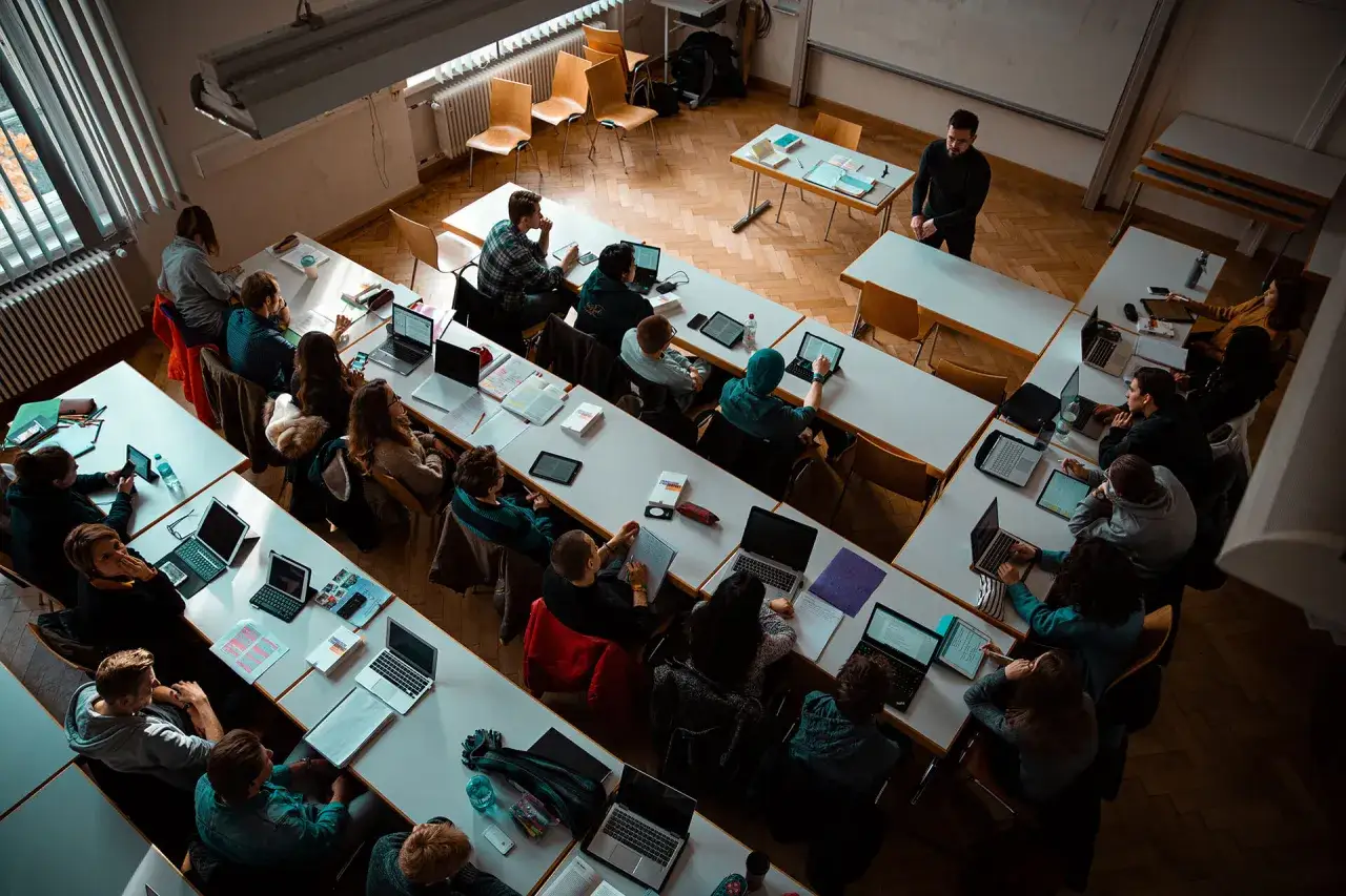 Studierende im **Fernstudium Theologie Evangelisch** hören aufmerksam zu. Laptops und Tablets liegen auf den Tischen.