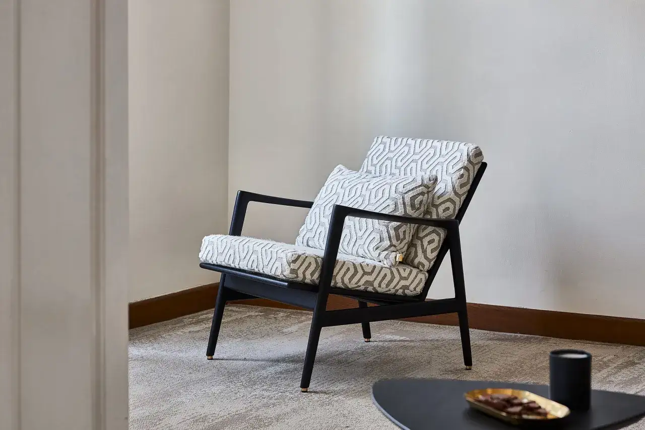 Elegancki fotel w stylu mid century modern z geometrycznym wzorem na poduszkach, idealny do stylowego salonu.