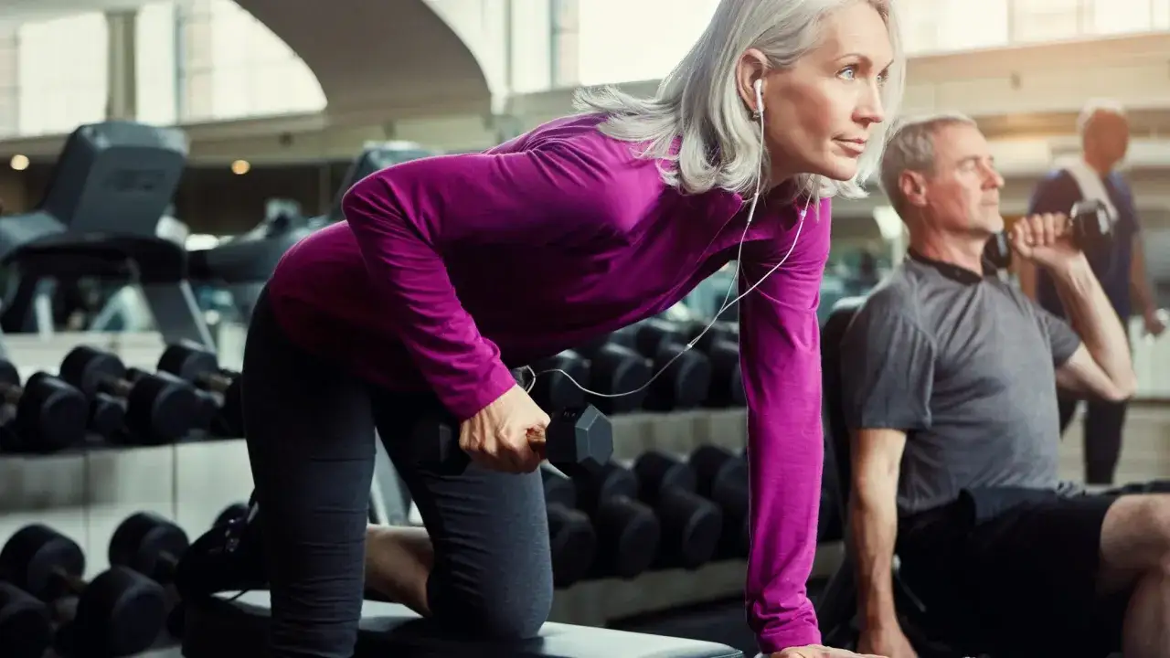 Donna con capelli grigi si allena in palestra con manubri, un esempio di come dimagrire in menopausa con attività fisica.