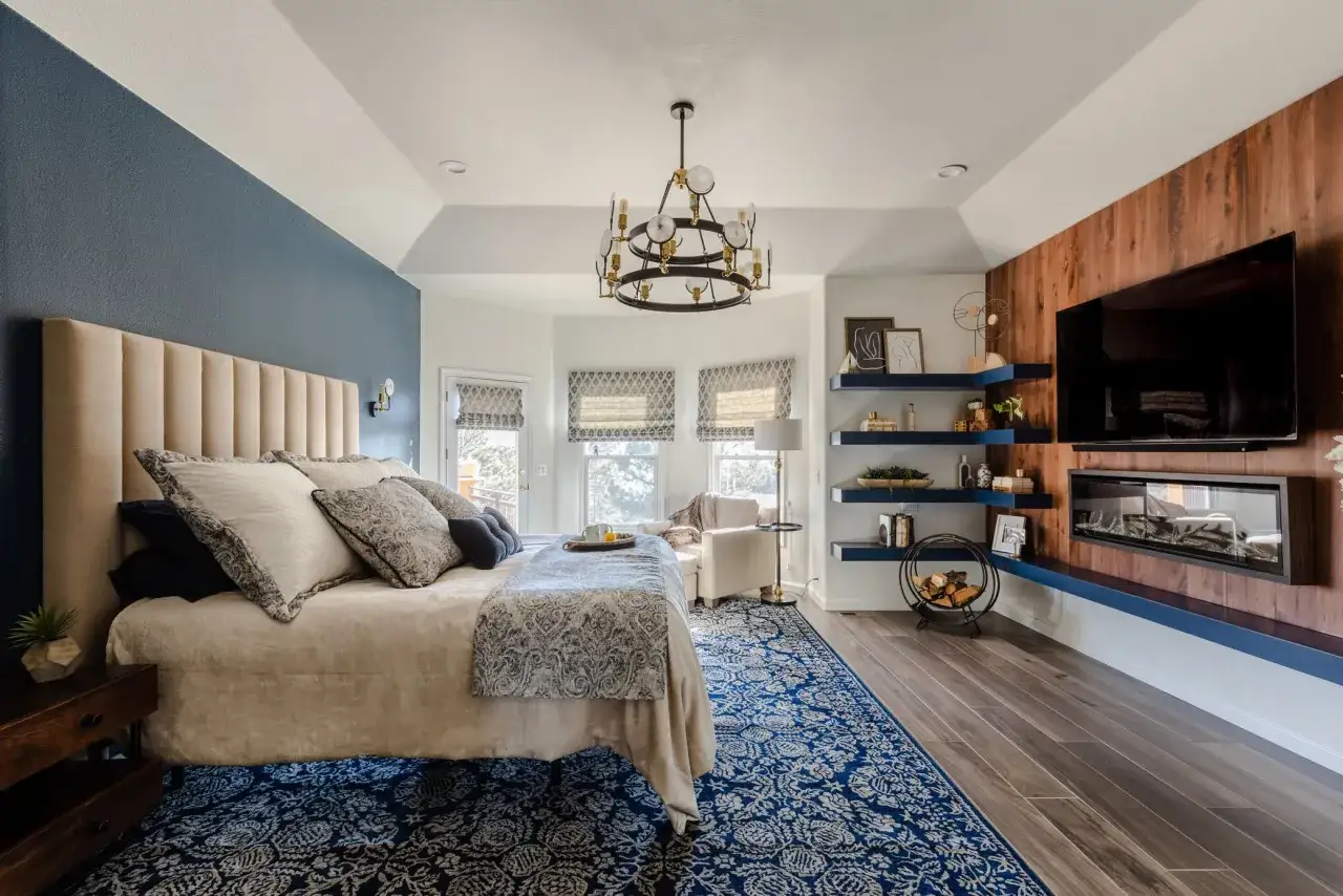 Elegante camera da letto blu con letto king-size, tappeto decorato e camino moderno.