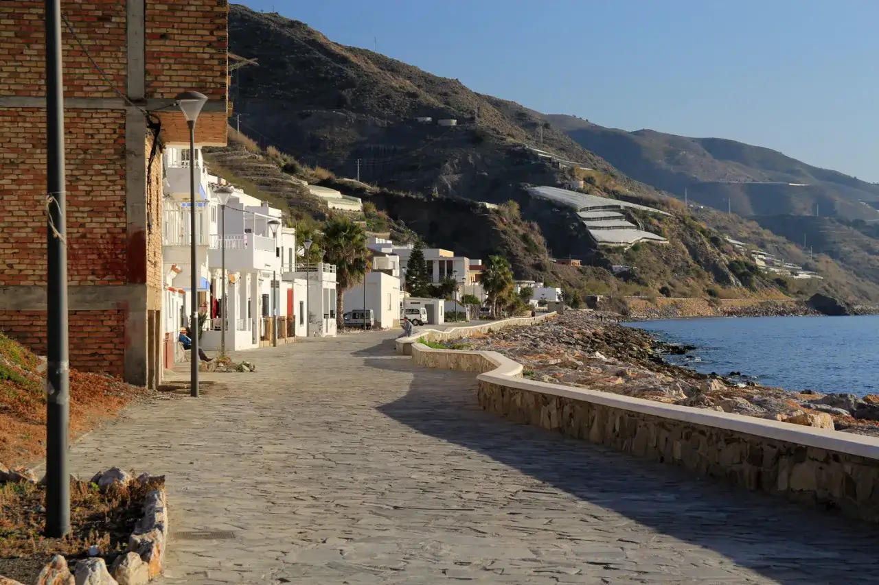 Paseo mar&iacute;timo de **playa los Yesos** con casas blancas, palmeras y monta&ntilde;as cubiertas de invernaderos al fondo.
