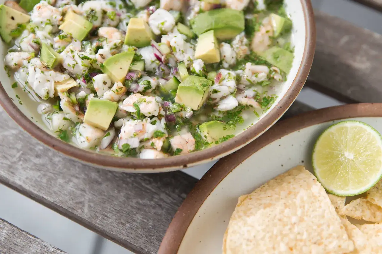 En skål med färsk ceviche med räkor, avokado och koriander. Perfekt för ett somrigt ceviche recept. Serveras med tortillachips och lime.