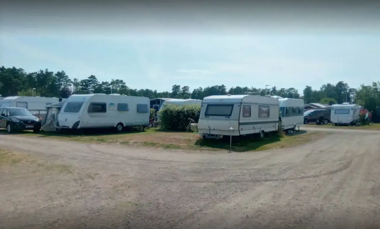 St&auml;llplatser med husvagnar och bilar p&aring; Olles camping. Tr&auml;d och bl&aring; himmel i bakgrunden.