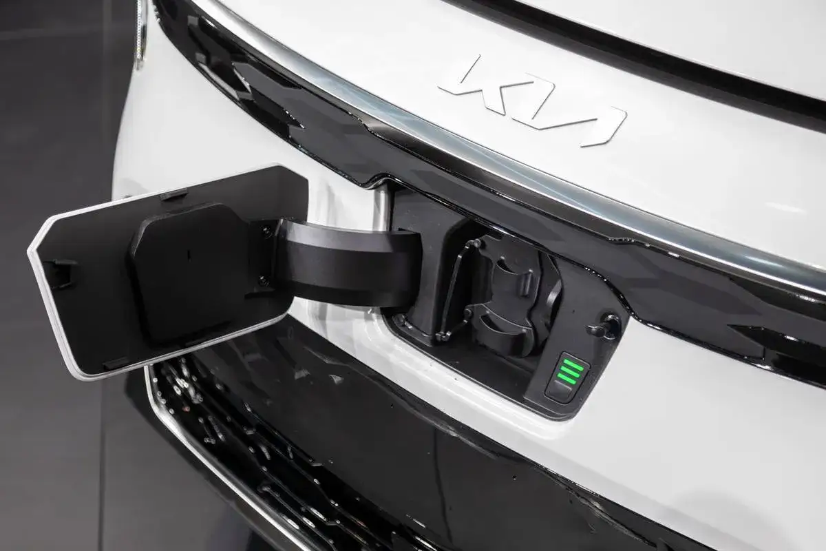 Otwarta klapka ładowania w białym Kia Niro EV. Wskaźnik naładowania pokazuje trzy zielone paski.