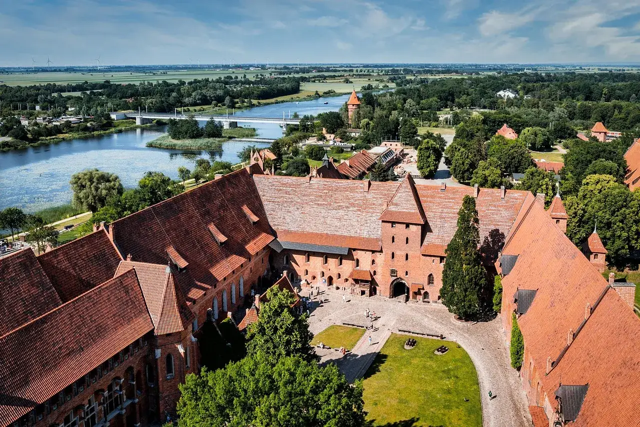 Malbork i okolice co zwiedzić? Potężny zamek krzyżacki nad rzeką Nogat, z malowniczymi dachami i dziedzińcami, zaprasza do odkrywania historii.