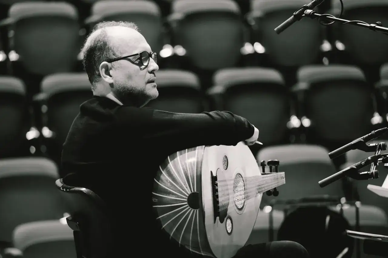 Anouar Brahem, w okularach, siedzi z oudem na kolanach, gotowy do koncertu.