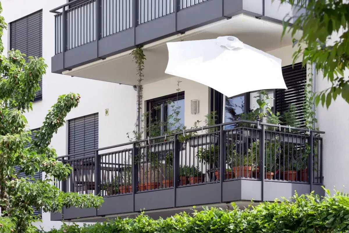 Nowe przepisy o balkonach i tarasach mogą wpłynąć na fundusz remontowy. Na zdjęciu nowoczesny balkon z roślinami i białym parasolem.