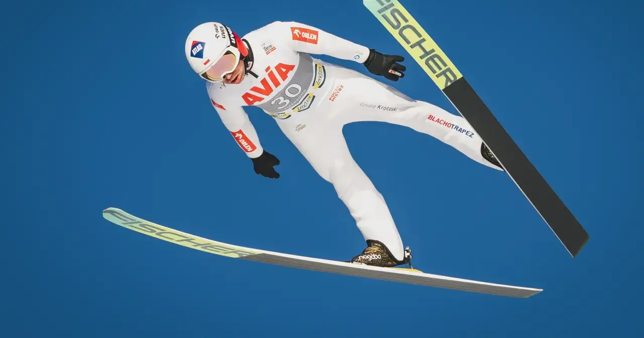 Skoki narciarskie dzisiaj: biały kombinezon, narty Fischer, kask z logo Atlas.