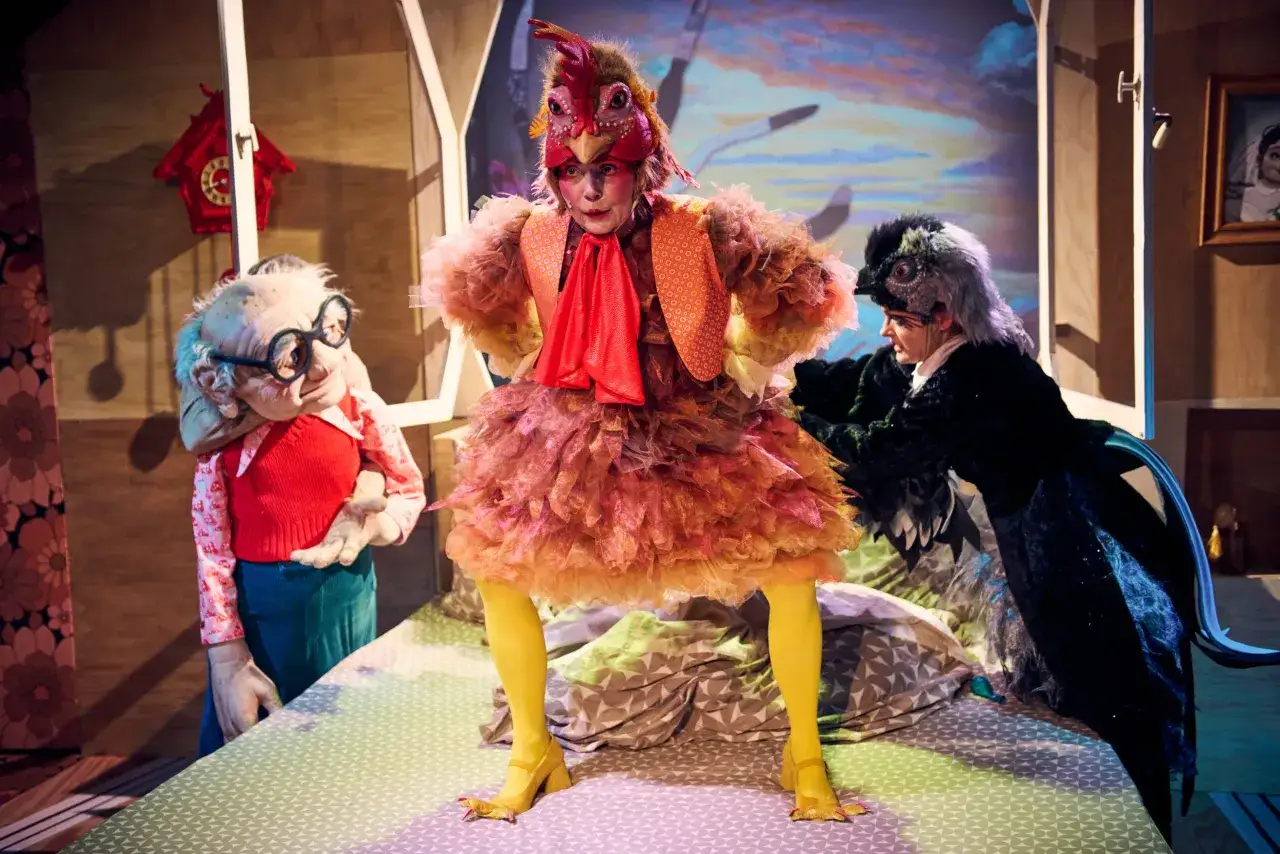 Trzy postacie w teatralnych kostiumach na scenie. W centrum kura, po bokach staruszek i ptak. Sprawdź repertuar Teatru Miejskiego w Gliwicach!