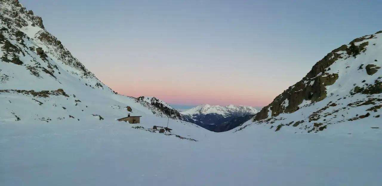 Alba sulle montagne innevate, con il bivacco Paolo e Nicola che appare come un rifugio accogliente tra i pendii.