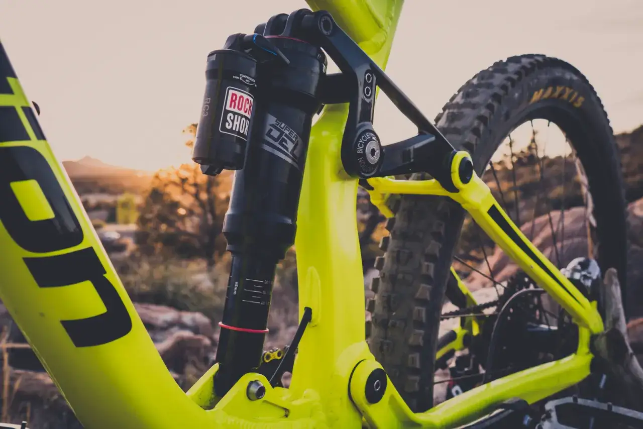 Close-up of a bright yellow mountain bike's rear suspension. The Rock Shox Super Deluxe shock has a length chart visible.