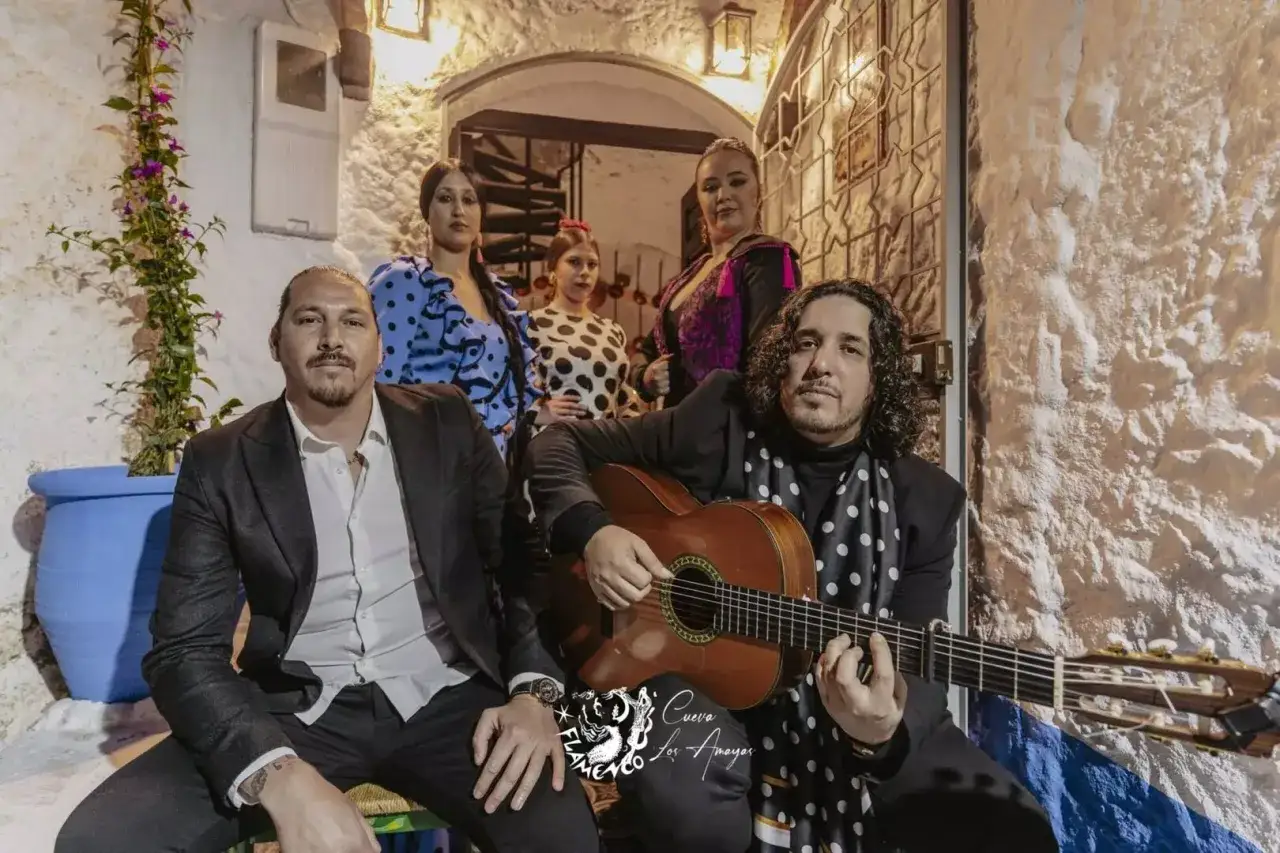 La familia Amaya, artistas de flamenco, posan con orgullo. Un guitarrista toca mientras las mujeres lucen trajes vibrantes.