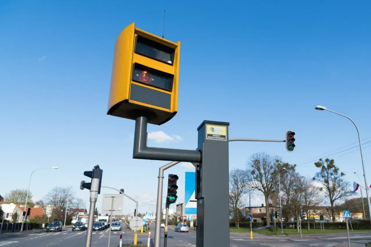 Żółty fotoradar nad drogą, obok sygnalizacji świetlnej. Pokazuje, jak działa fotoradar, monitorując ruch.
