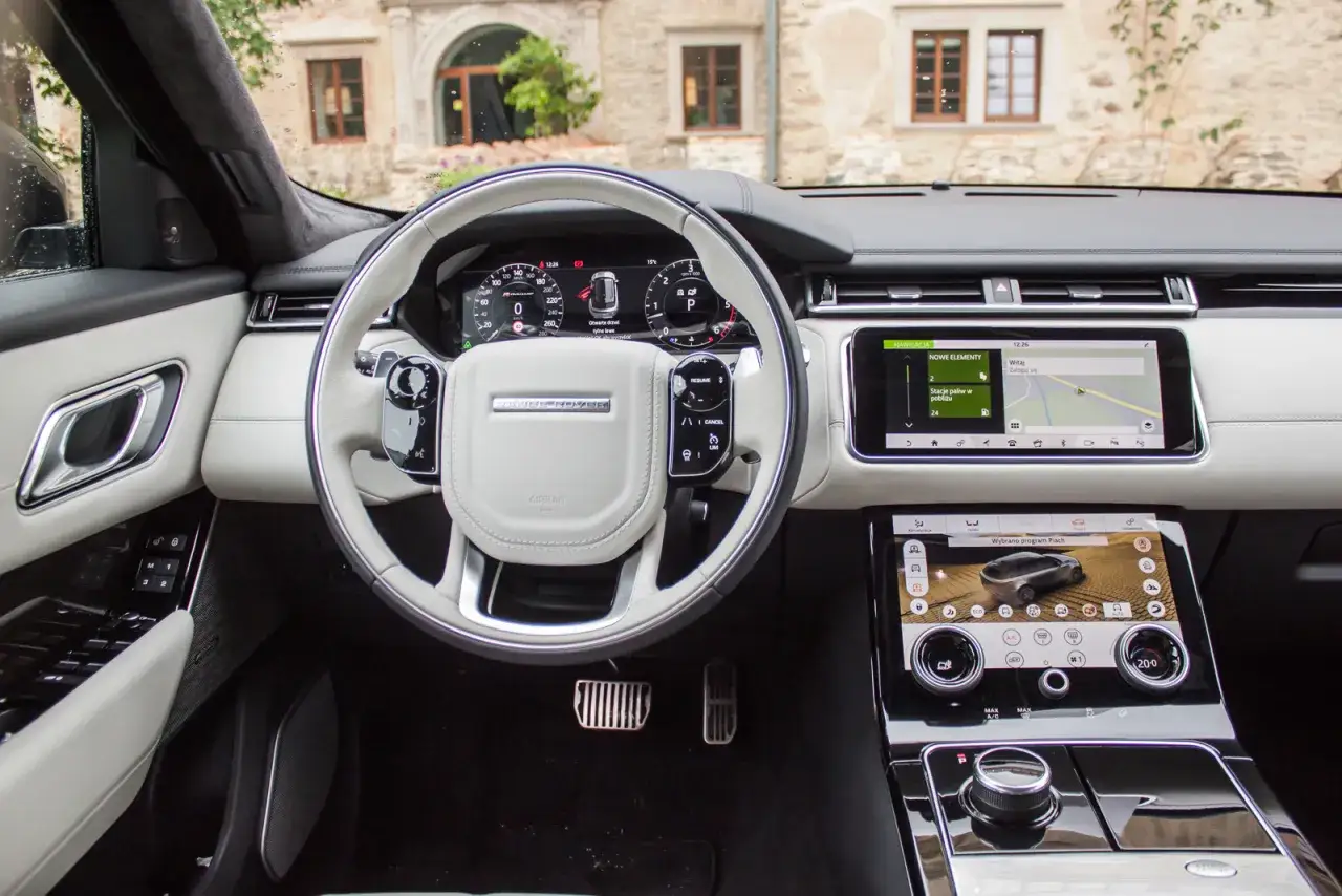 Wnętrze Range Rover Velar. Nawigacja pokazuje stacje paliw, sugerując potencjalną awaryjność lub potrzebę tankowania.