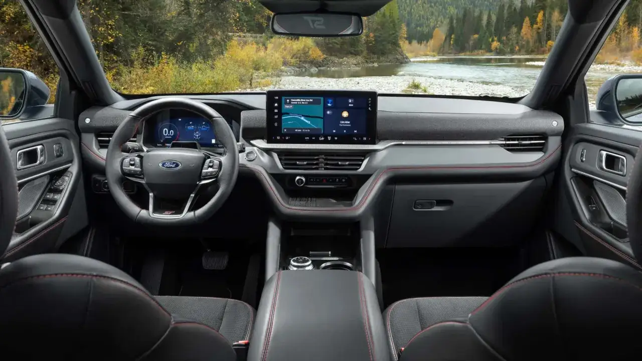 Wnętrze Ford Explorer ST z nowoczesnym ekranem multimedialnym i sportową kierownicą. Za oknem malowniczy krajobraz z rzeką i lasem.