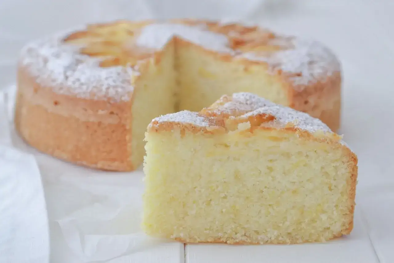Deliziosa torta con farina di riso, soffice e spolverata di zucchero a velo. Una fetta mostra la sua consistenza perfetta.