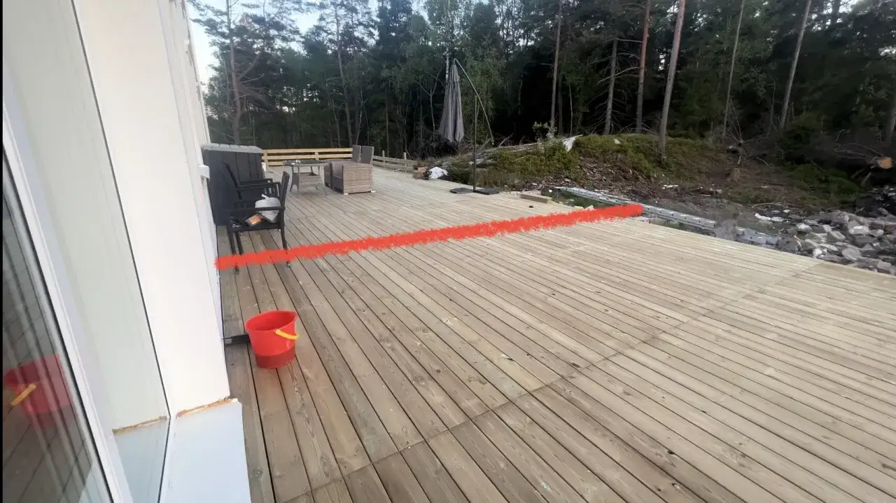 En altan med trädgårdsmöbler och en röd hink. En röd linje markerar var man ska bygga vindskydd.