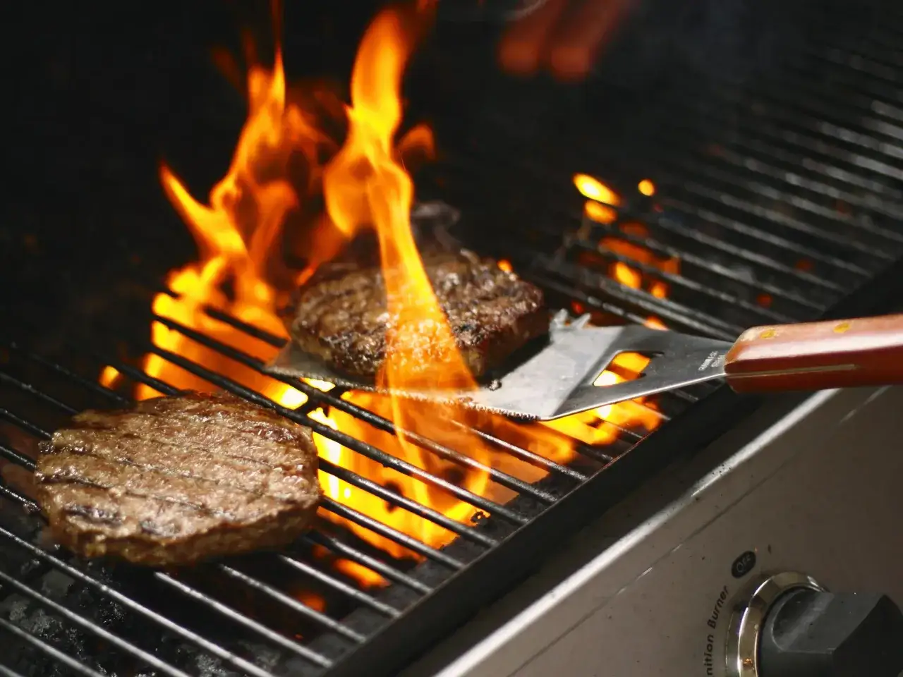 Deux steaks grillent sur un barbecue, entourés de flammes vives. La question est : combien de charbon pour un barbecue réussi ?