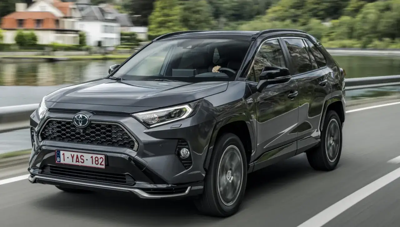 M&ouml;rkgr&aring; Toyota RAV4 k&ouml;rs p&aring; en v&auml;g med en sj&ouml; och hus i bakgrunden. En del av en toyota rav4 test.