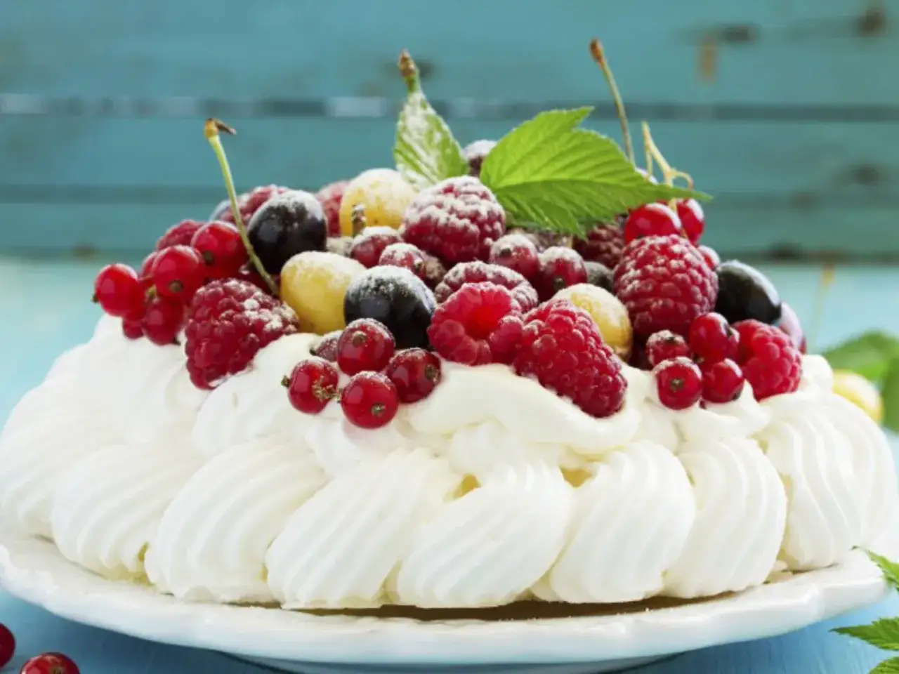 Ein k&ouml;stliches Pavlova-Rezept: Baiserhaube mit Schlagsahne und frischen Beeren, best&auml;ubt mit Puderzucker.